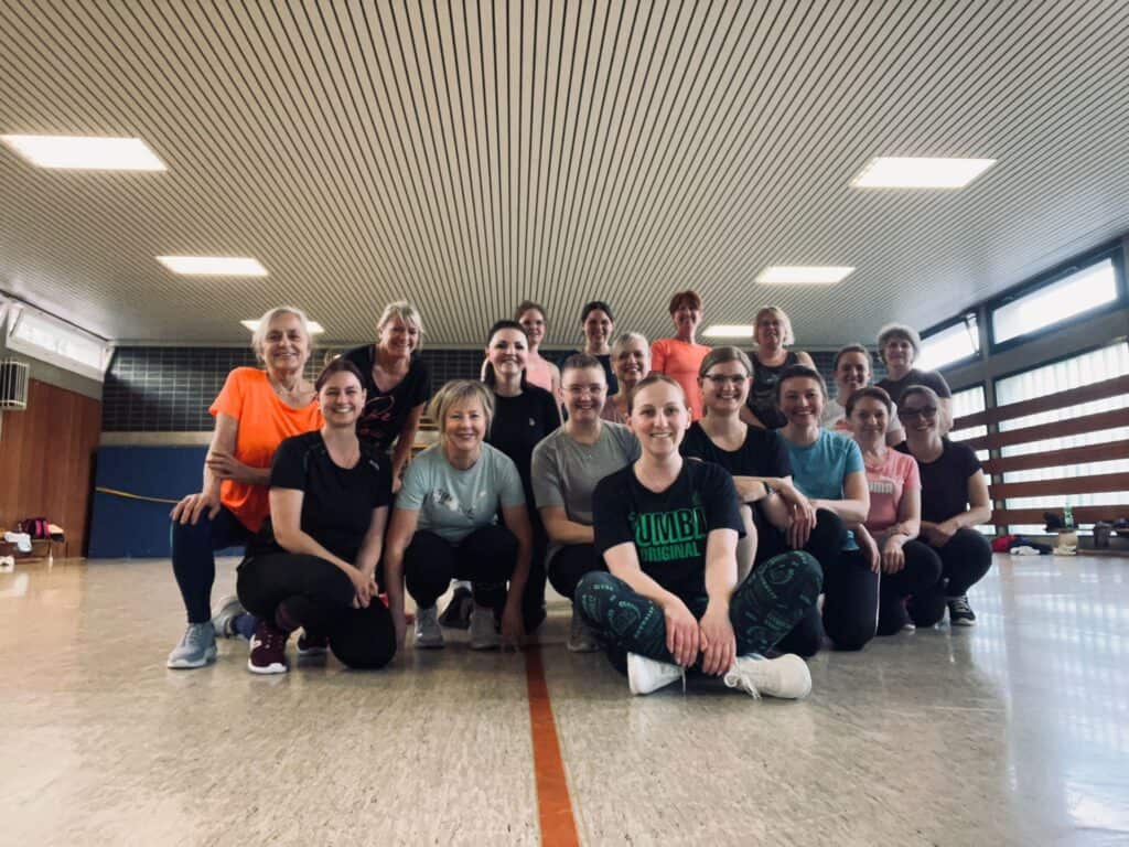 Showtanzgruppe Zumba mit einer Gruppe erwachsener Tänzerinnen bei einem gemeinsamen Gruppenfoto in einer Turnhalle.
